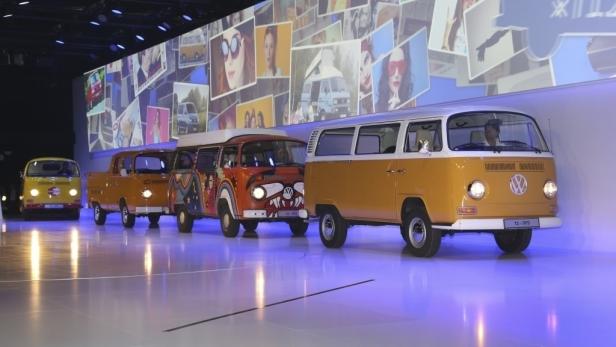 Mehrere gelbe VW-Busse stehen auf einer Bühne vor einer Fotowand.