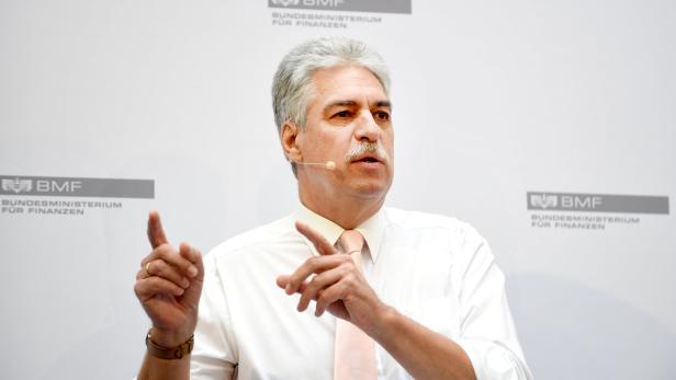 Ein Mann mit Mikrofon gestikuliert vor dem Logo des Bundesministeriums für Finanzen.