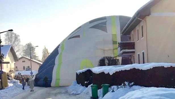 Ein Heißluftballon liegt teilweise auf einer verschneiten Straße in einem Wohngebiet.
