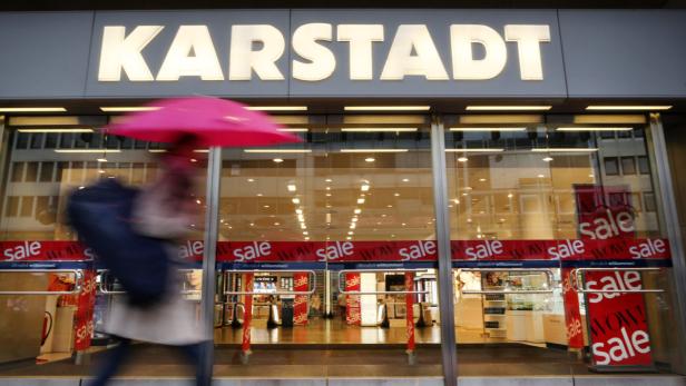 Eine Person mit einem Regenschirm geht an einem Karstadt-Kaufhaus vorbei, das mit „Sale“-Schildern dekoriert ist.