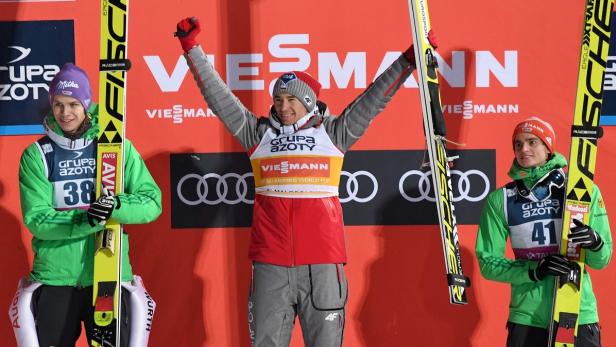 Drei Skispringer stehen auf dem Siegerpodest, der Gewinner jubelt mit erhobenen Armen.
