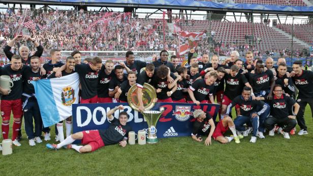 Die Fußballmannschaft von Red Bull Salzburg feiert den Double-Gewinn 2014 mit Pokal und Fans im Hintergrund.