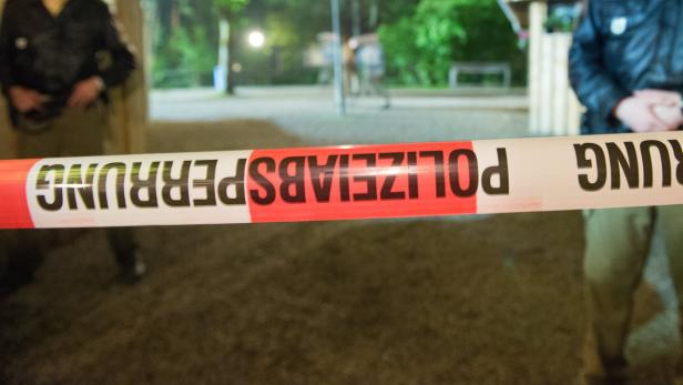 Ein rot-weißes Absperrband der Polizei vor unscharfen Personen im Hintergrund.