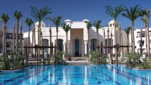 Ein luxuriöses Resort mit einem großen Pool und vielen Palmen unter blauem Himmel.
