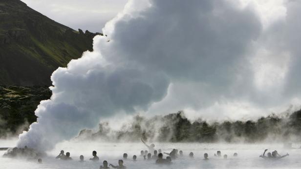 Menschen baden in der Blauen Lagune in Island, aus der Dampf aufsteigt.