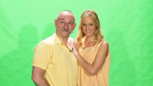 Ein Mann mit Schnurrbart und eine blonde Frau stehen vor einem grünen Hintergrund.