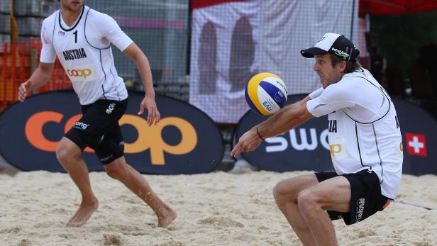 Zwei Beachvolleyballspieler aus Österreich bei einem Spiel im Sand.