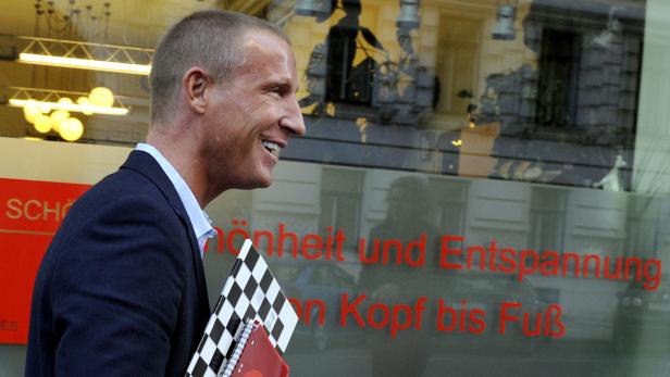 Ein lächelnder Mann in einem Anzug geht an einem Schaufenster vorbei.