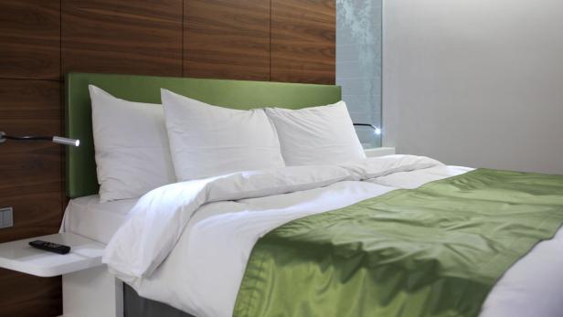 Ein Doppelbett mit weißer Bettwäsche und einer grünen Tagesdecke.