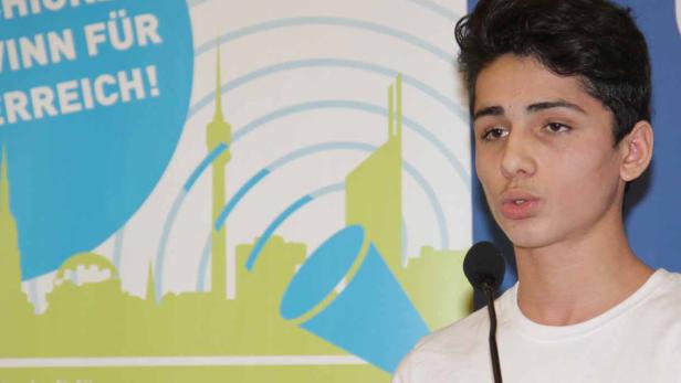 Ein junger Mann spricht vor einem Mikrofon, im Hintergrund ein Logo zum Thema Integration.