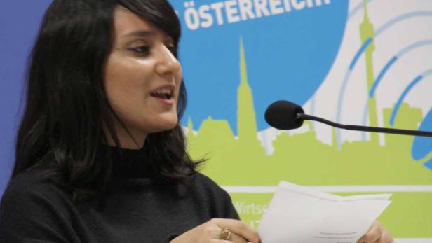 Eine Frau spricht an einem Rednerpult mit Mikrofon vor einem Hintergrund mit der Aufschrift „Mehr Gewinn für Österreich!“.