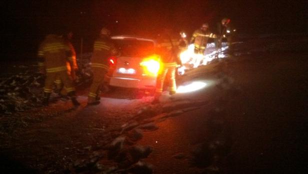 Feuerwehrleute arbeiten nachts an einem verunglückten Auto.