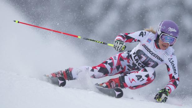 Eine Skirennläuferin fährt einen Hang hinunter, umgeben von Schneestaub.