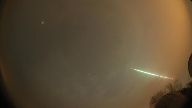 Ein Meteor zieht als heller Streifen über den Nachthimmel.