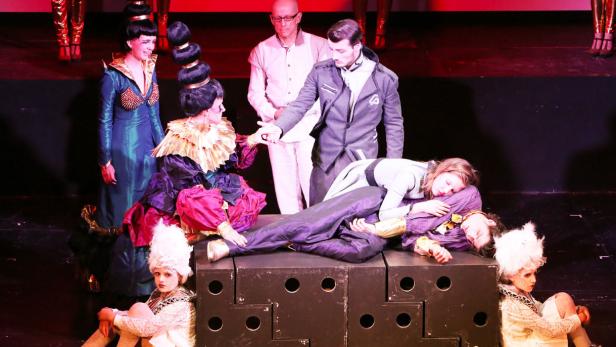 Eine Theaterszene mit aufwendigen Kostümen und einer Gruppe von Schauspielern auf einer Bühne.