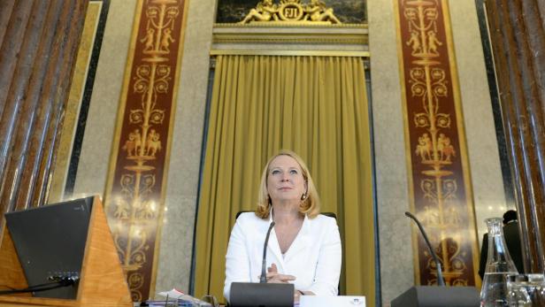 Eine Frau sitzt an einem Tisch vor einem goldenen Vorhang.