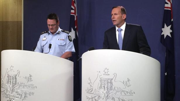 Ein Polizist und ein Mann im Anzug stehen an Rednerpulten mit australischen Wappen.
