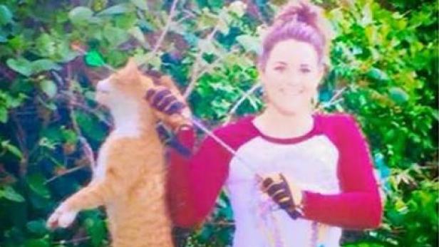 Eine Frau hält eine Angelrute, während eine orangefarbene Katze daneben steht.