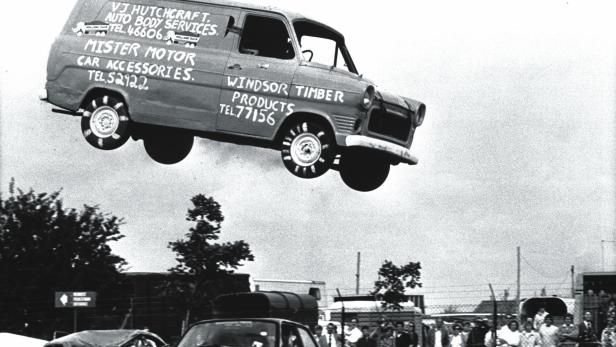Ein Lieferwagen springt über ein Auto vor einer Menschenmenge.