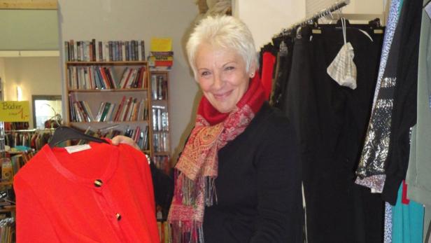 Eine lächelnde Frau mit rotem Schal hält eine rote Strickjacke in einem Secondhand-Laden.