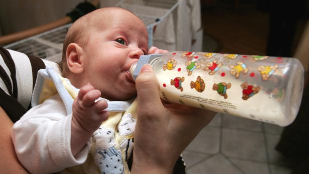 Ein Baby trinkt Milch aus einer mit Teddybären verzierten Flasche.