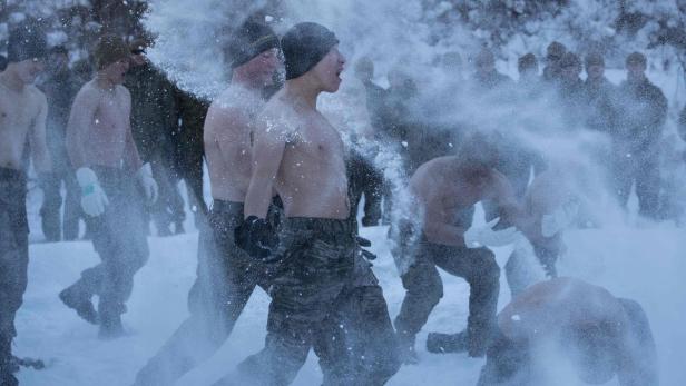 Eine Gruppe von Männern, einige mit freiem Oberkörper, wirft im Schnee mit Schnee um sich.
