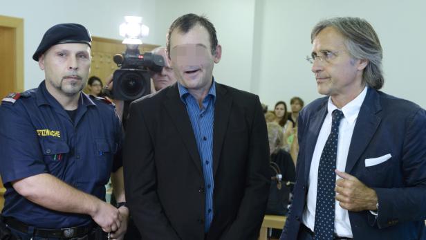 Ein Mann mit verpixelten Gesicht wird von einem Justizbeamten und einem Anwalt flankiert.