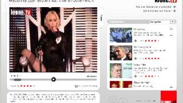 Madonna sitzt auf einem Stuhl und singt in ein Mikrofon während eines Live-Auftritts.