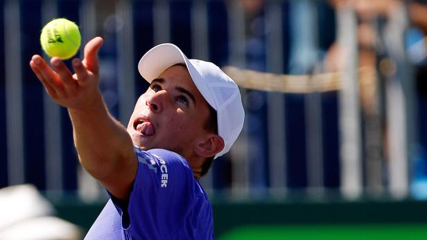 Ein Tennisspieler mit weißer Kappe wirft einen Tennisball hoch.