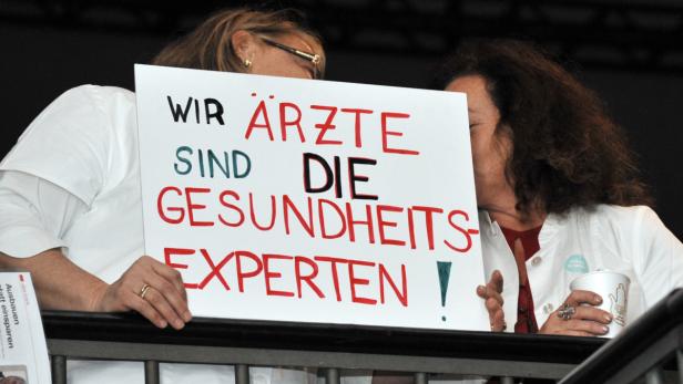 Zwei Ärztinnen halten ein Schild mit der Aufschrift „Wir Ärzte sind die Gesundheitsexperten!“.