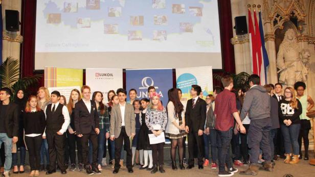 Eine Gruppe von Jugendlichen steht auf einer Bühne vor Bannern und Flaggen.