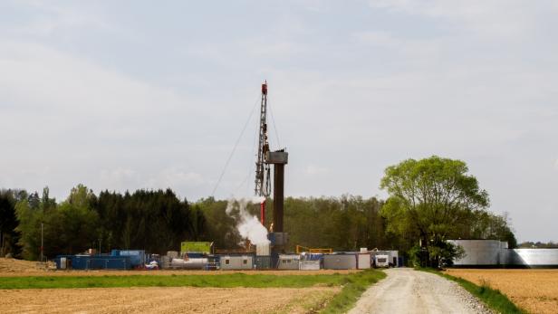 Eine Ölbohranlage steht auf einem Feld, aus dem Rohre ragen und Dampf austritt.