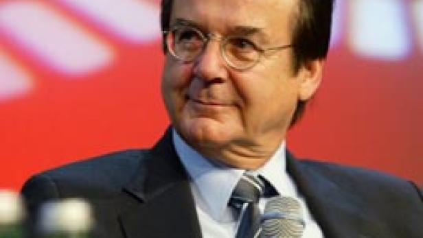 Ein Mann mit Brille und Anzug hält ein Mikrofon in der Hand.