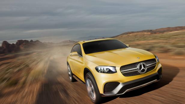 Ein gelber Mercedes-Benz fährt auf einer staubigen Straße in einer Wüstenlandschaft.