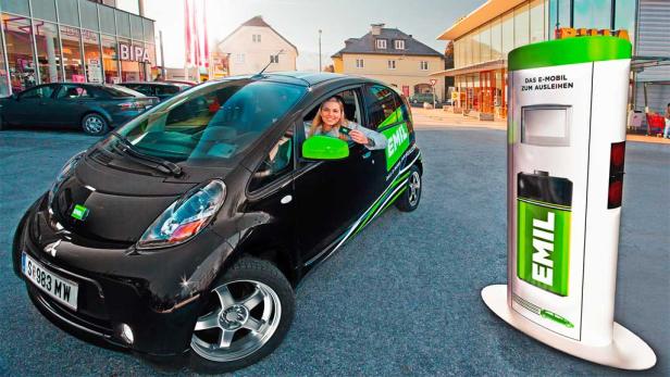 Eine Frau sitzt in einem schwarzen Elektroauto der Marke „Emil“ und hält eine Karte in der Hand.