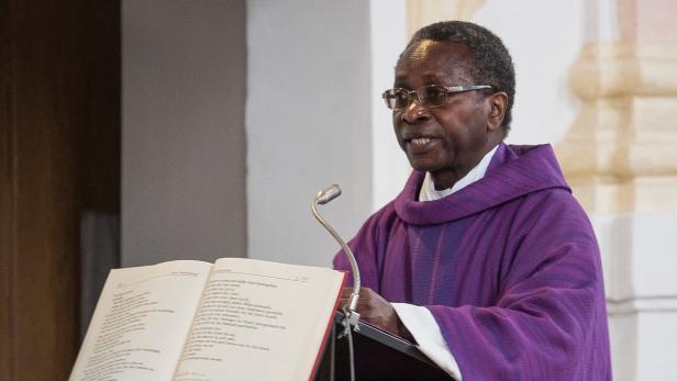 Ein Priester in lila Gewändern liest aus einem Buch vor einem Mikrofon.