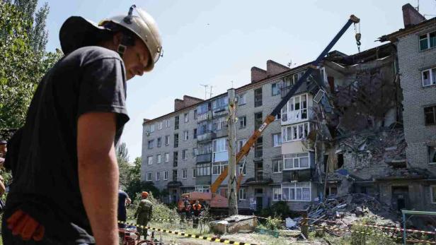 Ein beschädigtes Wohngebäude mit Trümmern und ein Kran bei Aufräumarbeiten.