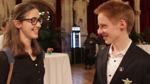 Eine junge Frau mit Brille und ein junger Mann im Anzug unterhalten sich lächelnd.