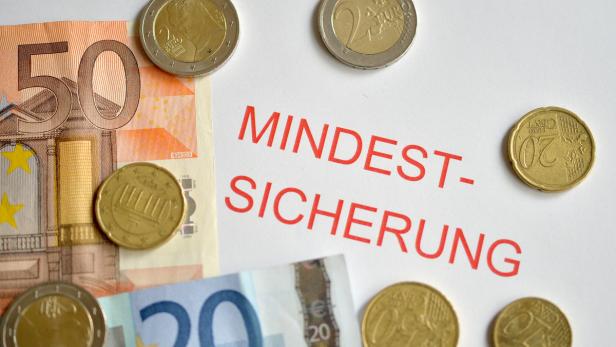 Euro-Banknoten und Münzen liegen neben dem roten Schriftzug „Mindestsicherung“.