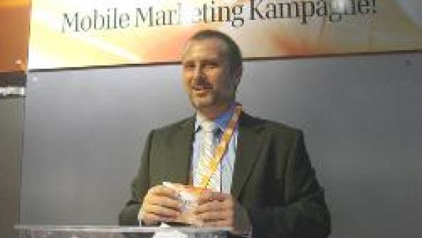 Ein Mann steht vor einem Losbehälter mit der Aufschrift „Gewinnen Sie die 100.000 Euro Mobile Marketing Kampagne!“.