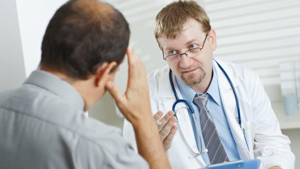 Ein Arzt spricht mit einem Patienten, der seine Hand an die Stirn hält.