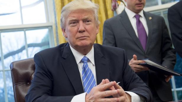 Donald Trump sitzt an einem Tisch mit gefalteten Händen.