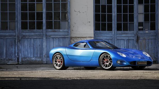 Ein blauer Toroidion-Sportwagen steht vor einer blauen Holztür.