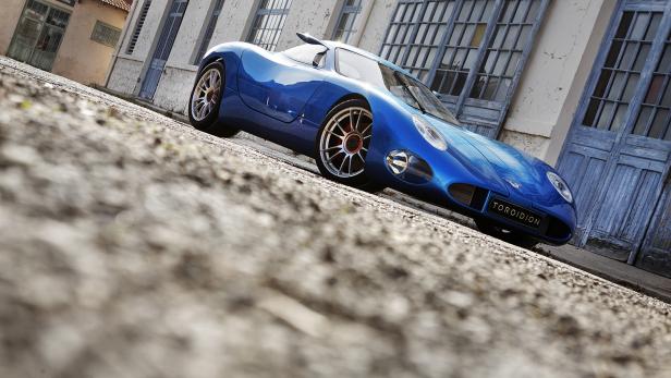 Ein blauer Toroidion-Sportwagen steht vor einem Gebäude mit blauen Fensterläden.