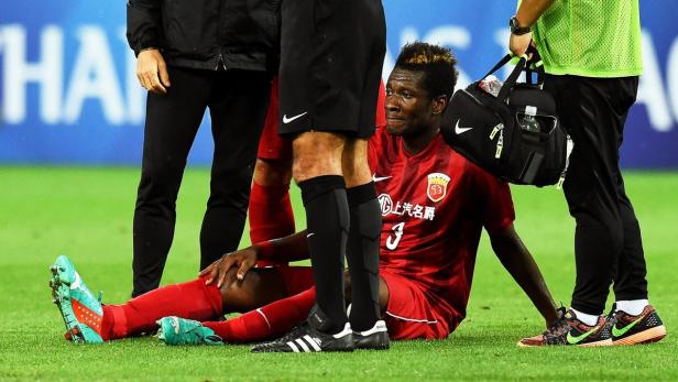 Ein Fußballspieler sitzt verletzt auf dem Rasen, umgeben von Betreuern.