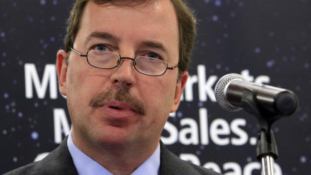 Ein Mann mit Brille und Schnurrbart steht vor einem Mikrofon.