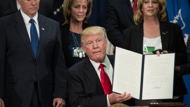 Trump hält seine Unterschrift hoch.