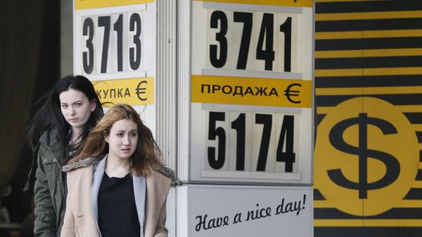 Zwei Frauen stehen vor einer Wechselkurstafel mit Euro- und Dollarzeichen.