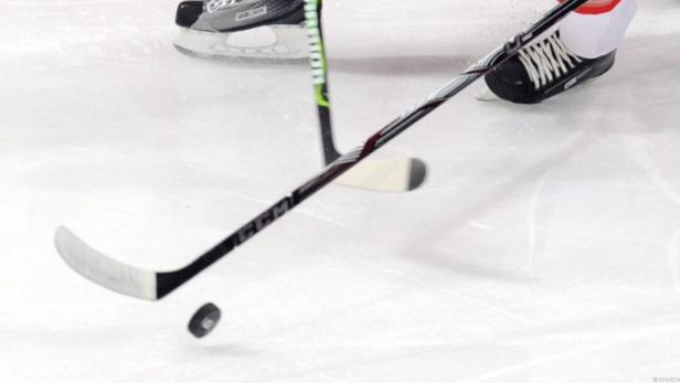 Ein Eishockey-Puck liegt auf dem Eis neben zwei Eishockeyschlägern.