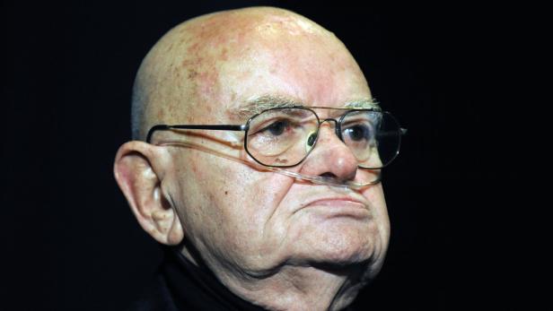 Ein älterer Mann mit Glatze und Sauerstoffbrille blickt ernst.